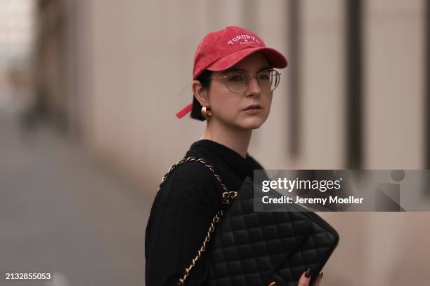 Maria Barteczko seen wearing Ray-Ban gold round retro glasses, Pull&Bear red vintage baseball cap, WENDYKEI black wrinkled oversized midi dress,...