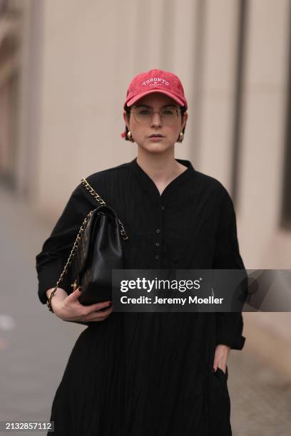 Maria Barteczko seen wearing Ray-Ban gold round retro glasses, Pull&Bear red vintage baseball cap, WENDYKEI black wrinkled oversized midi dress,...