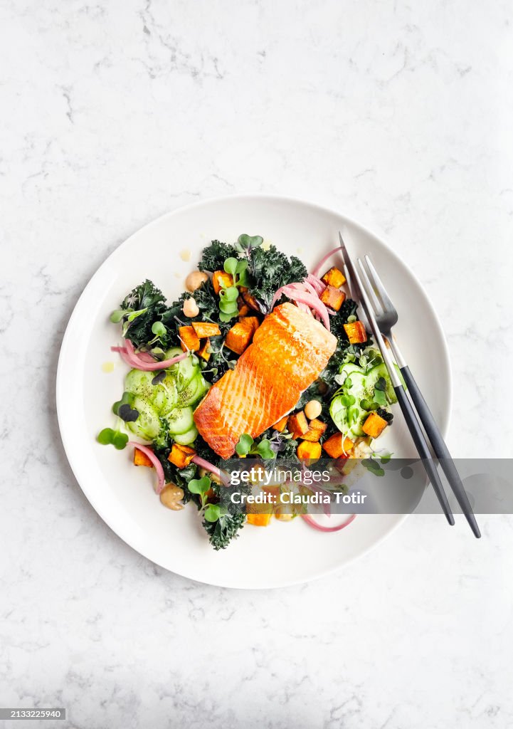 Plate of pan roasted salmon with fresh salad on white background