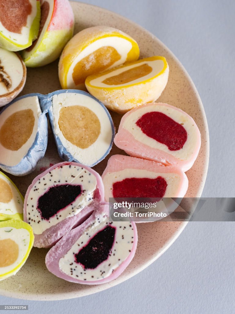 A plate of Japanese mochi, each one cut in half to reveal the colorful filling inside. The colorful mochis feature different fillings such as ice cream or fruit paste inside the outer shell.