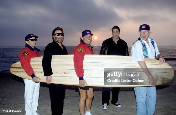 American musicians Al Jardine, Carl Wilson , Bruce Johnston, Brian Wilson and Mike Love, of the American rock band The Beach Boys, carry a surfboard...