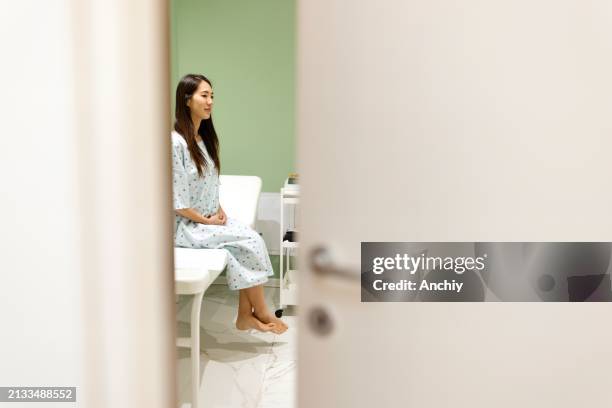 patient attendant seul en blouse assis sur une table d’examen. - blouse dexamen médical photos et images de collection