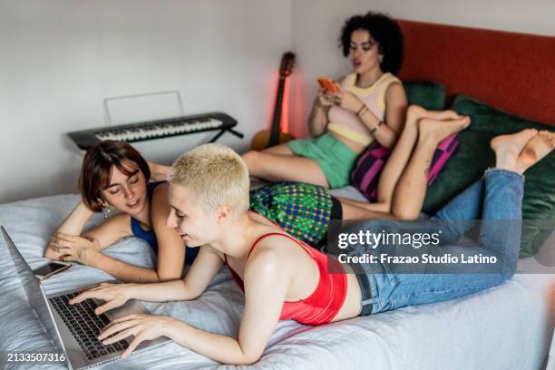 amigos que usan una computadora portátil acostada en la cama en casa - compañero de vivienda fotografías e imágenes de stock
