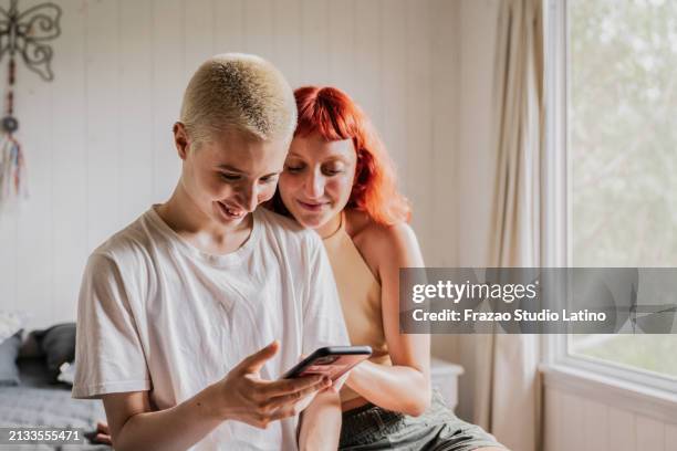 female friends using mobile phone on bedroom at home - alternative lifestyle stock pictures, royalty-free photos & images
