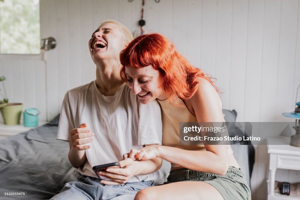 Female friends using mobile phone on bedroom at home