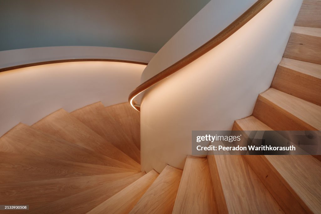 A contemporary spiral staircase with a flawless white balustrade and warm wooden steps.