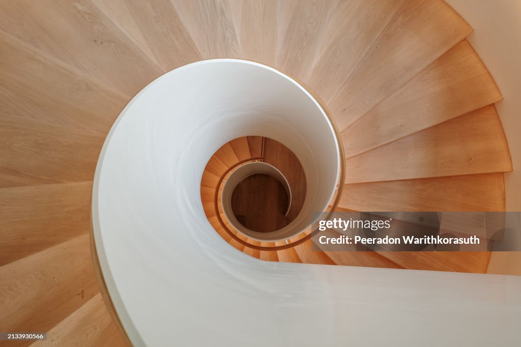 A contemporary spiral staircase with a flawless white balustrade and warm wooden steps.
