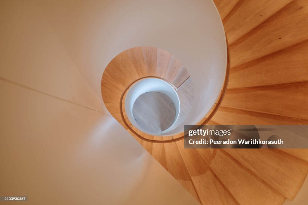 A contemporary spiral staircase with a flawless white balustrade and warm wooden steps.