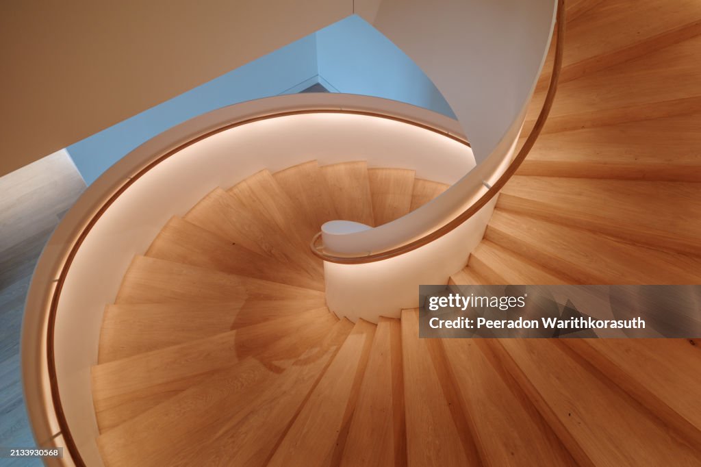 A contemporary spiral staircase with a flawless white balustrade and warm wooden steps.