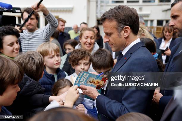 French President Emmanuel Macron signs an autograph on Adolph Huxley's book "Brave New World" during a visit to the Ecole primaire d'application...