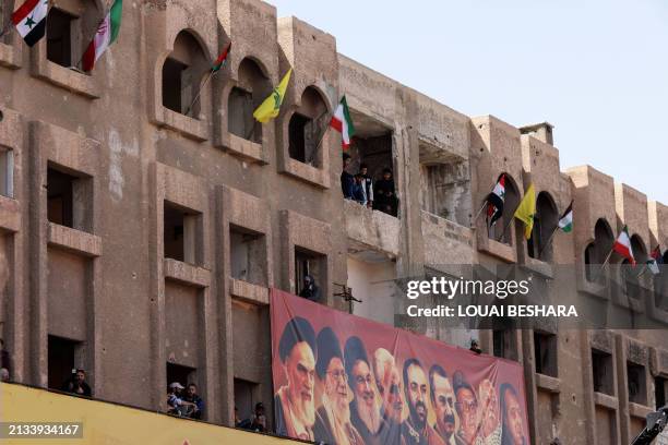 Banner bearing pictures of Iranian and pro-Iran leaders as well as flags hang on the facade of a damaged building, during a military parade to mark...