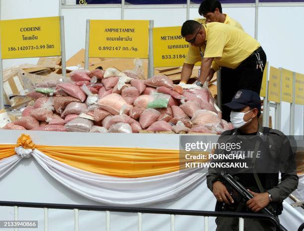 Policeman stands guard while officials unpack haul of methamphetamines, heroin, opium, ecstasy, cocaine and marijuana for burning in Ayutthaya...