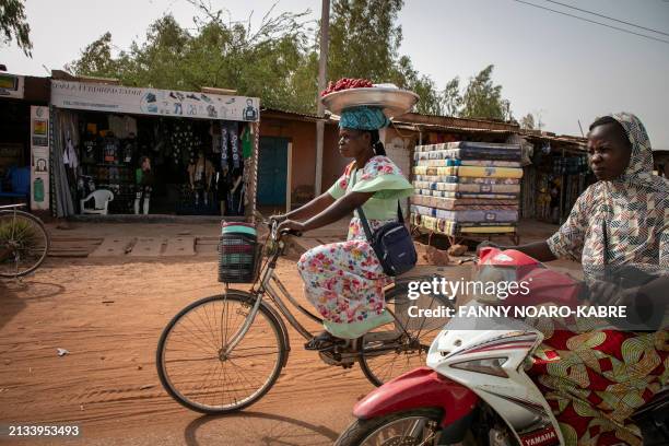 Jacqueline Taonsaon balances a plate of strawberries on her head as she rides on her bicycle to the market in Ouagadougou on March 28, 2024. In the...
