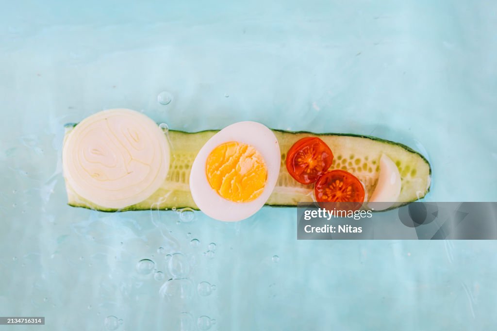 Creative composition of gazpacho ingredients: cucumber with garlic egg and cherry tomato looks like a boat in water. Healthy food concept