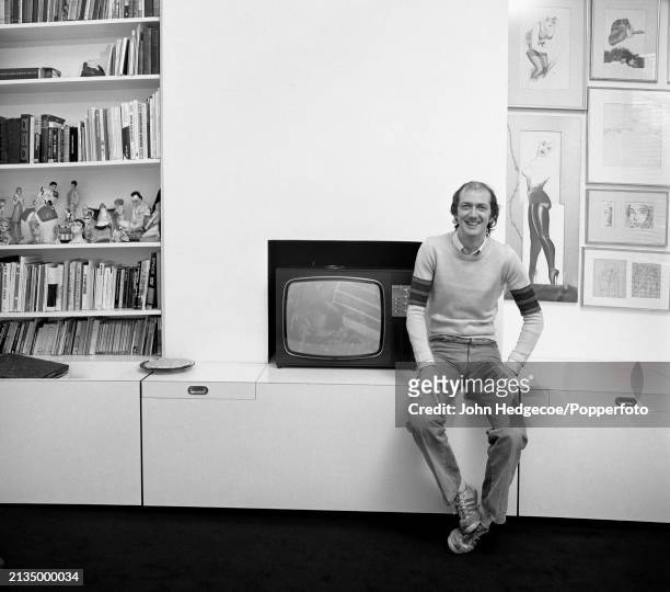 English pop artist Allen Jones seated beside a television in a living room decorated with a selection of his own paintings and prints, at home in...