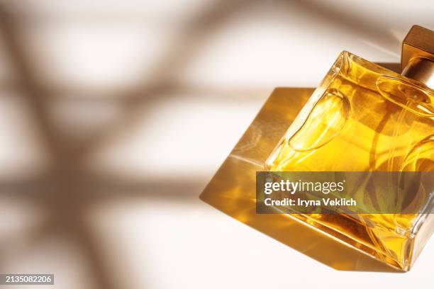 make-up cosmetic product for a woman glass bottle perfume in a glass transparent bottle with caustic light effect on white beige color background with shadow from sunlight. - dark peach color stock pictures, royalty-free photos & images