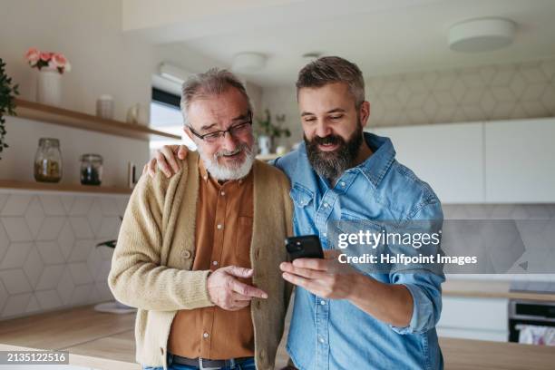 mature son showing dad photos of his family in smartphone, making video call. - dementia father stock pictures, royalty-free photos & images