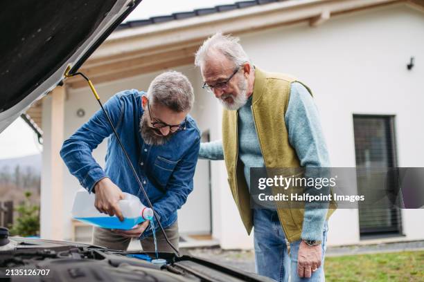 elderly father teaching son how to refill fluid in a car, coolant in radiator, windshield washer fluid for sprayers. home car maintenance. - scheibenwischer stock-fotos und bilder
