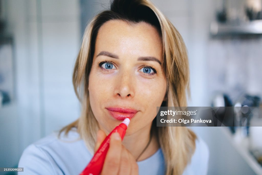 Mature middle-aged woman applying lipstick makeup, close-up, lip gloss