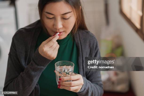 woman taking a pill, close up of asian woman taking medicine dietary supplements, vitamins, or medicines for treating various diseases at home - acetylsalicylizuur stockfoto's en -beelden