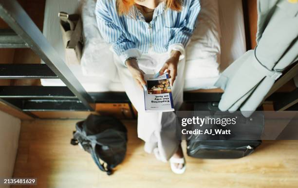young woman sitting in a hostel dorm and reading a travel guide - guidebook stock pictures, royalty-free photos & images
