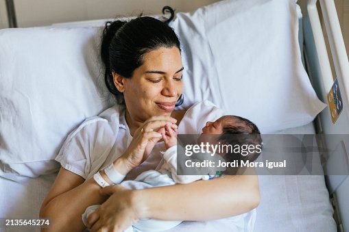 Woman holds the hands of her newborn baby as she rests in a hospital bed. Woman holds the hands of her newborn baby as she rests in a hospital bed.