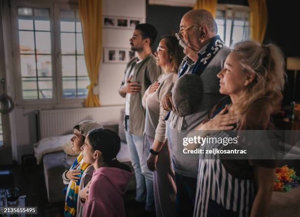 multigeneration family football fans singing national anthem at home - national womens soccer league stock pictures, royalty-free photos & images