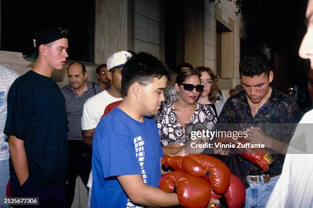 Mexican-American boxer Oscar De La Hoya among a group of people signs boxing gloves as he attends a boxing program at the Great Western Forum in...