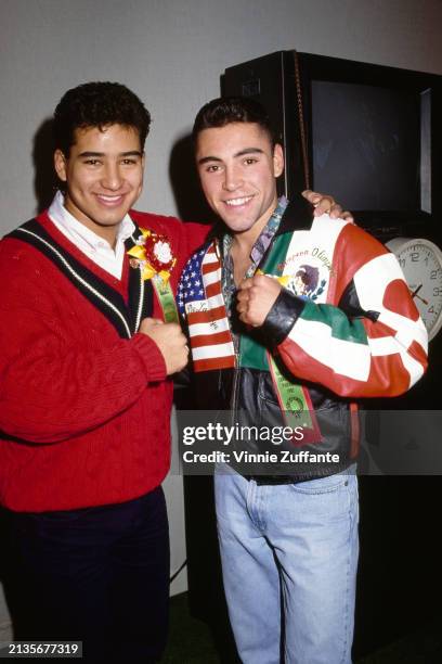 American actor Mario Lopez, wearing a red v-neck sweater over a white shirt, and Mexican-American boxer Oscar De La Hoya, who wears a leather jacket...