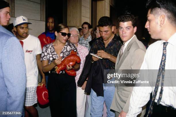 Mexican-American boxer Oscar De La Hoya among a group of people signs boxing gloves as he attends a boxing program at the Great Western Forum in...