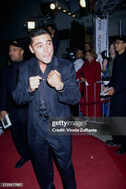 Mexican-American boxer Oscar De La Hoya, wearing a black pinstripe suit over a black shirt, pulls his cuff back to show his Swatch wristwatch at the...