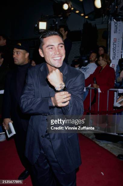 Mexican-American boxer Oscar De La Hoya, wearing a black pinstripe suit over a black shirt, pulls his cuff back to show his Swatch wristwatch at the...