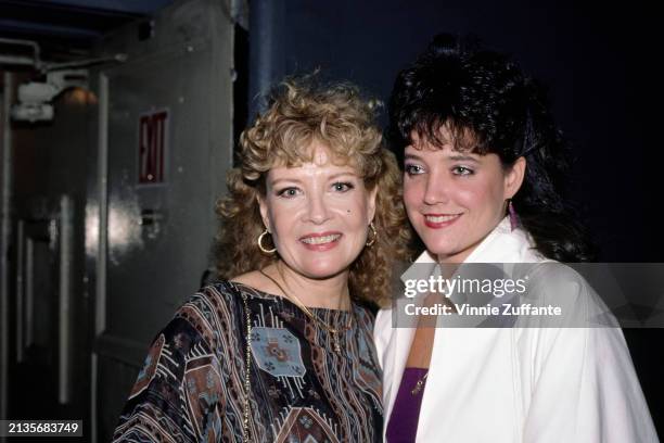 American actress and singer Gloria DeHaven, wearing a brown-and-blue patterned outfit, with her daughter, Faith Fincher, who wears a white jacket...