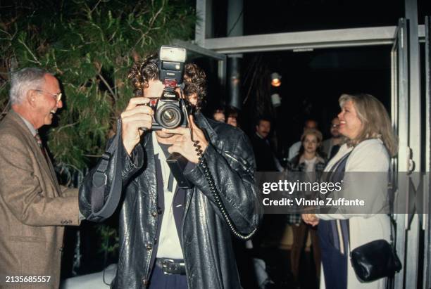 American actor Patrick Dempsey, who wears a leather jacket over a blue suit and white shirt, holds a Canon SLR camera, at the West Hollywood premiere...