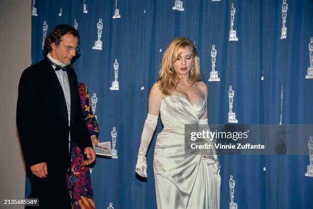 American actor Christopher Lloyd, wearing a tuxedo and bow tie, and American actress Rebecca De Mornay, who wears a strapless white evening gown with...