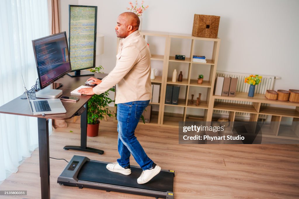 Black Man is Working at Home Office and Walking on Under Desk Treadmill
