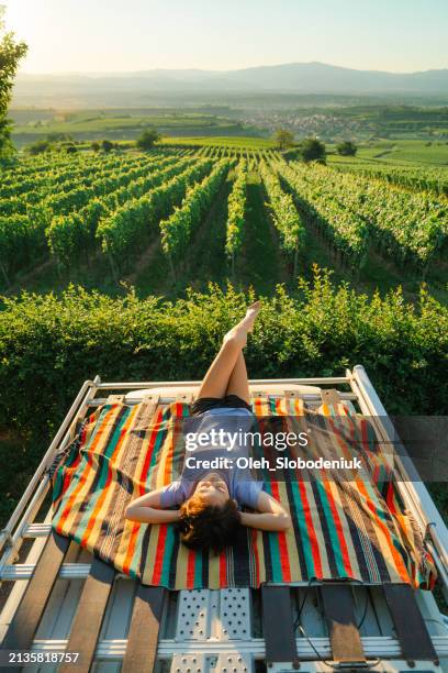 woman laying on the rooftop of camper van at vineyards - agritourism stock pictures, royalty-free photos & images