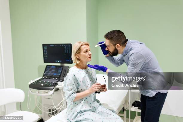 arzt, der dem patienten mit einem ophthalmoskop in die augen schaut - ophthalmoskop stock-fotos und bilder