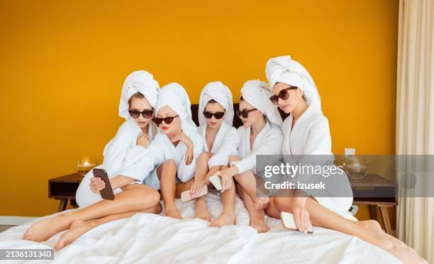 female friends wearing white bathrobes and towels on heads sitting on bed and taking selfie - hotel room white bed stock pictures, royalty-free photos & images