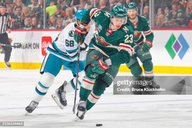 Marco Rossi of the Minnesota Wild skates with the puck while Mike Hoffman of the San Jose Sharks defends during the game at the Xcel Energy Center on...