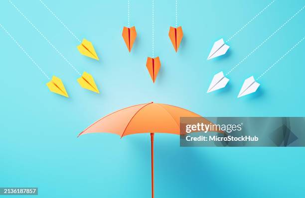 aeroplanini di carta che volano verso un ombrello color corallo su sfondo blu - difendere foto e immagini stock