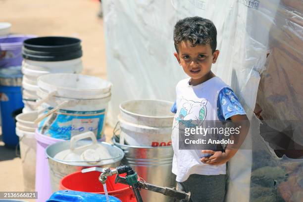 Palestinian child wait fills buckets and plastic containers with water at the fountain as Palestinians wait in water lines to fill their water jugs...