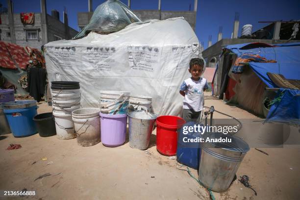 Palestinian child wait fills buckets and plastic containers with water at the fountain as Palestinians wait in water lines to fill their water jugs...