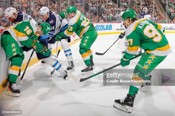 Dylan Samberg and Logan Stanley of the Winnipeg Jets battle for the puck along the boards with Mats Zuccarello, Marco Rossi and Kirill Kaprizov of...