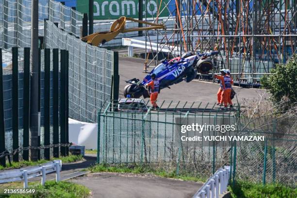 Officials remove the car of RB's Australian driver Daniel Ricciardo from the track after he crashed out at the start of the Formula One Japanese...