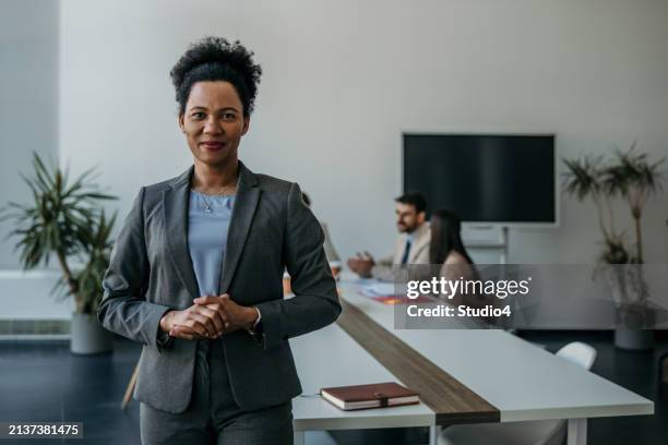 confident businesswoman standing tall, exuding leadership amidst a bustling office meeting - exuding stock pictures, royalty-free photos & images