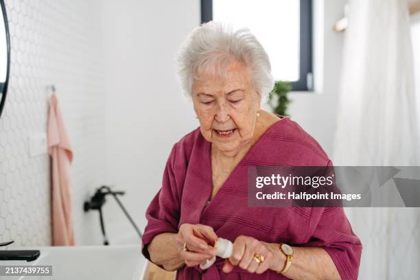 elderly woman doing skincare routine in bathroom, applying moisturise cream on face. senior woman putting sunscreen lotion on before going outdoors. - putting sunscreen stock pictures, royalty-free photos & images