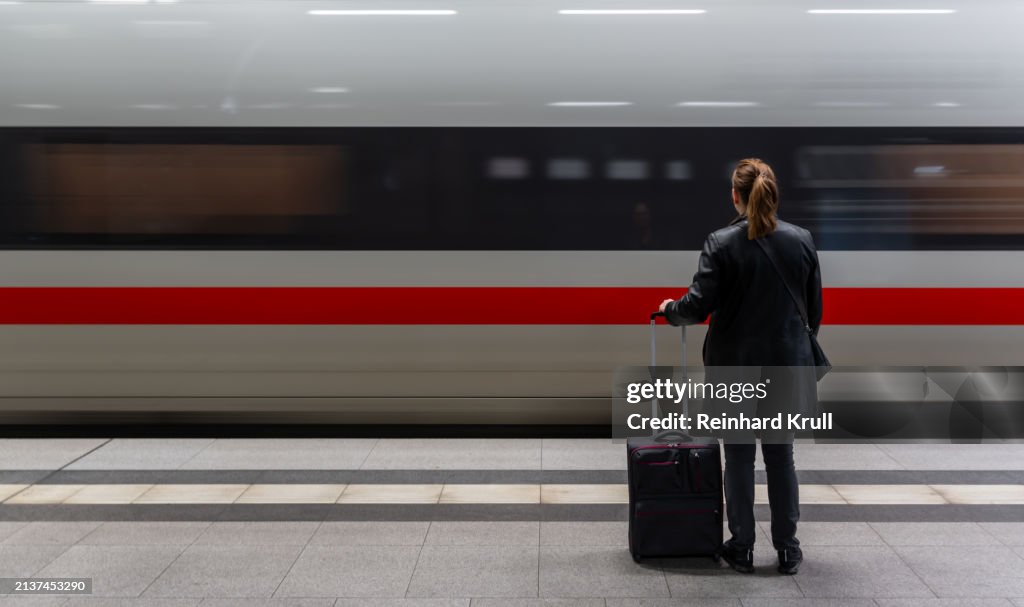 Rear view of woman with luggage standing in front of arriving passenger train