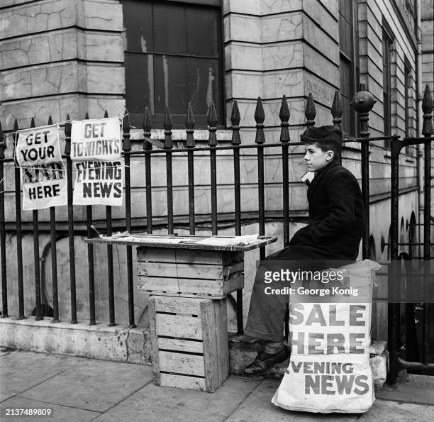Boy watches over a newspaper vendor's stall at an unspecified location in London, February 1949. Posters attached to the railings read 'Get your Star...