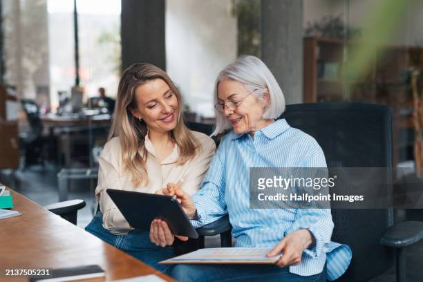 portrait of two female colleagues in various age groups in office. older manager as mentor for new female employee. age diverse team concept. - may december romance stock pictures, royalty-free photos & images